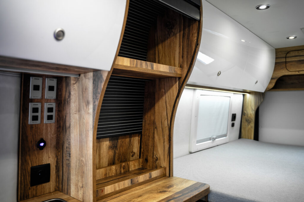Wnętrze kampera z drewnianymi półkami, łóżko